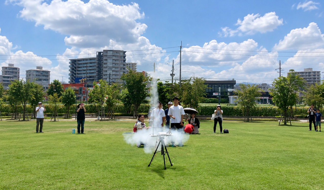芝生の広場でモデルロケットの打ち上げを見守る参加者